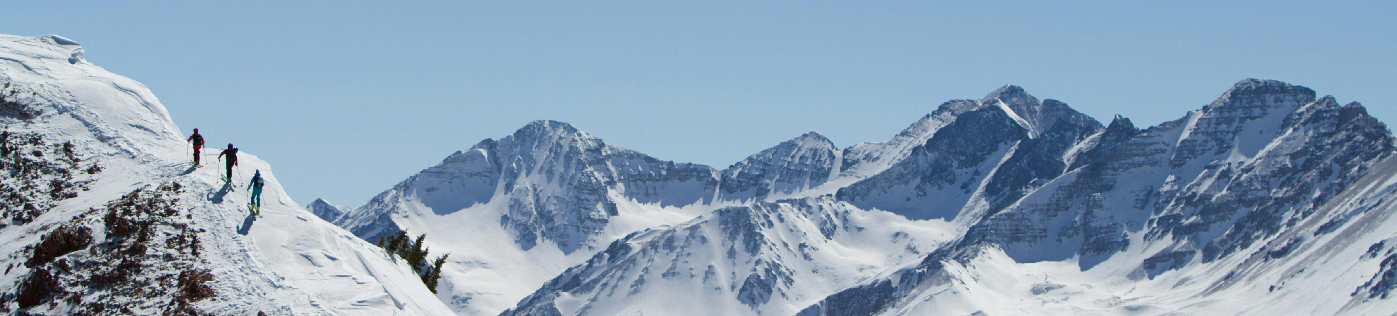 Three skiers traverse a mountain ridge